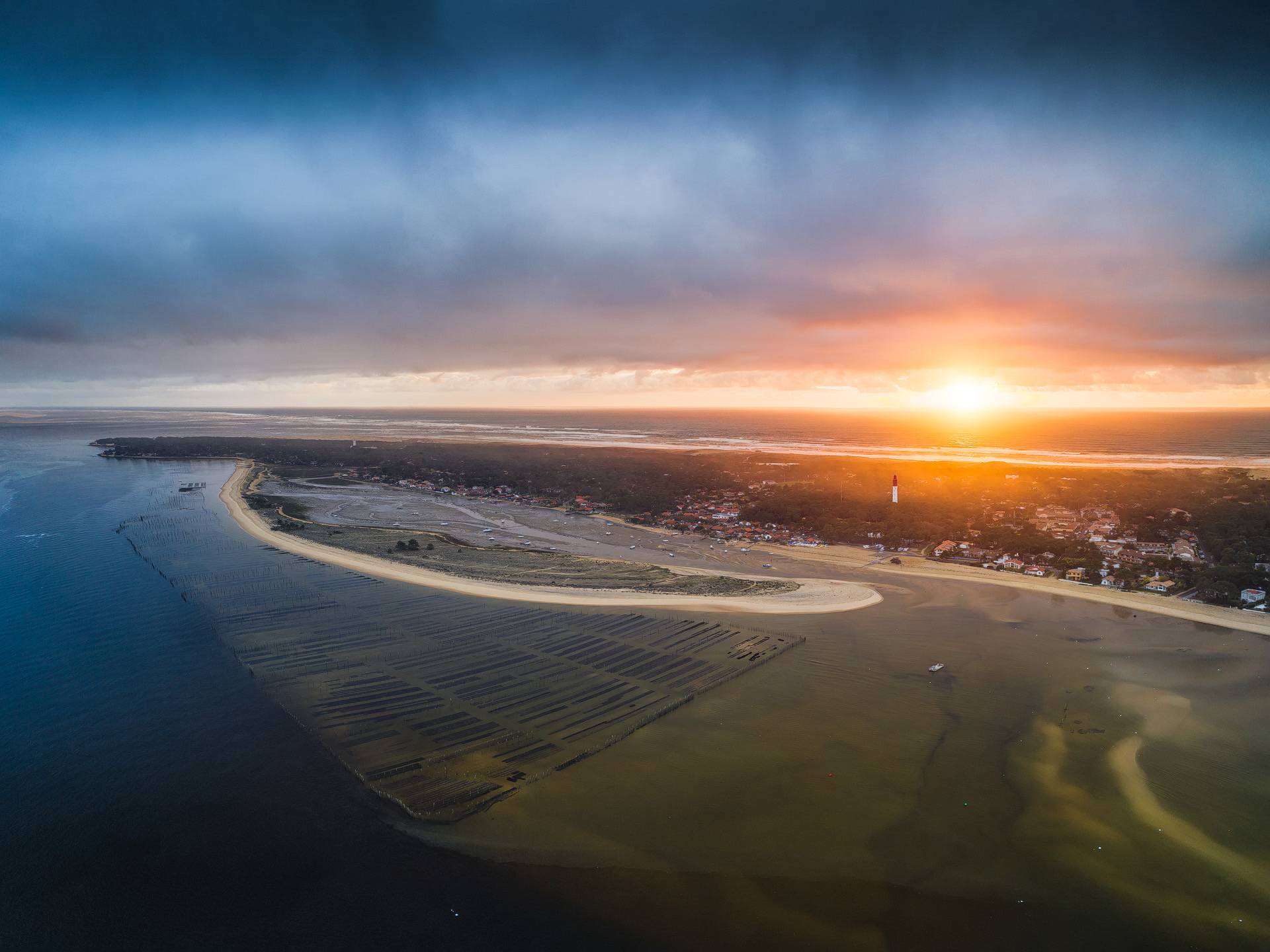 Photo aérienne du coucher du soleil au dessus du Mimbeau avec le phare du Cap Ferret en arrière plan